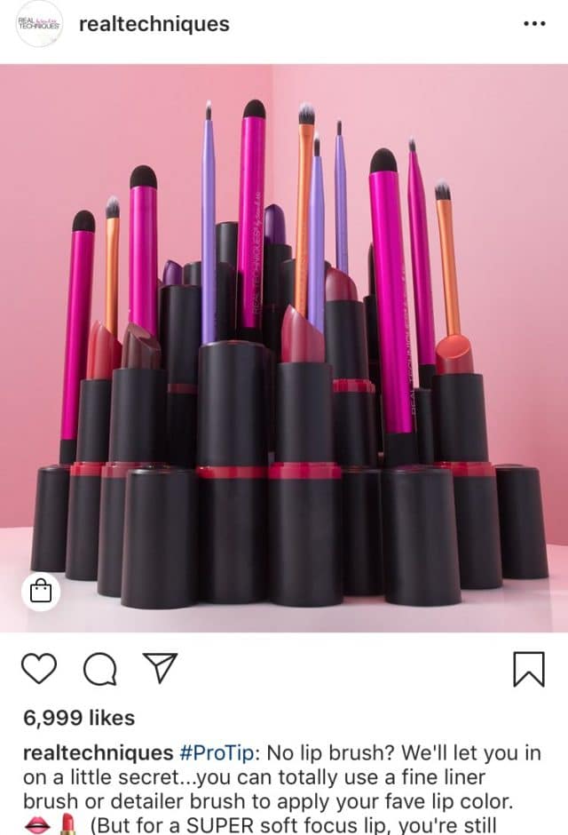 The Real Techniques Instagram post shows several makeup brushes and lipsticks sitting upright over a pink background.